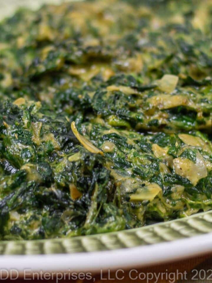 Creamed Spinach wit Artichoke on a green and white serving platter.