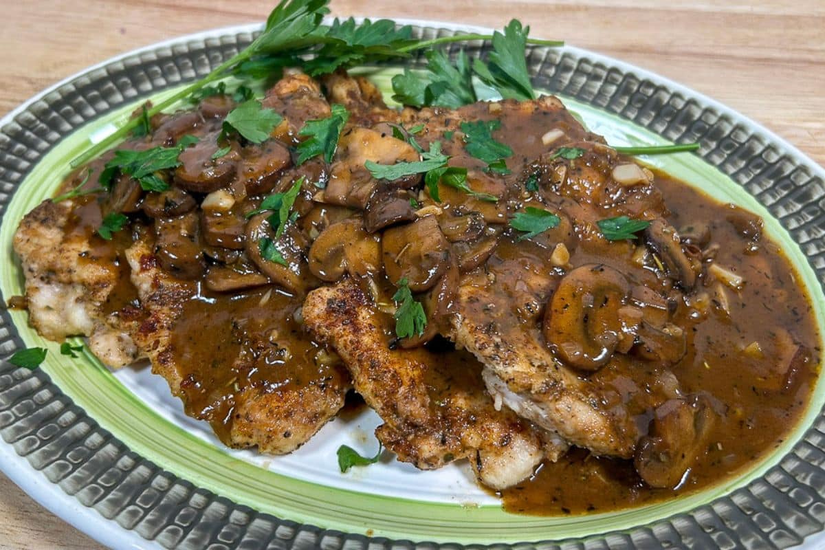 Mushroom Gravy over chicken breasts on a green and white serving platter with garnish.