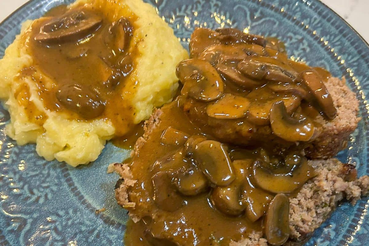 Mushroom Gravy over garlic mashed potatoes and meatloaf on a blue-green dinner plate.