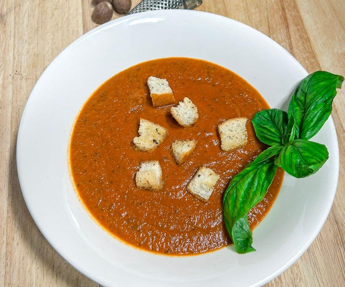 Tomato Basil Bisque in a white bowl with croutons and basil garnish.