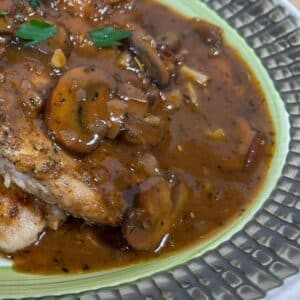 Mushroom Gravy poured over chicken breasts on a serving platter with garnish.