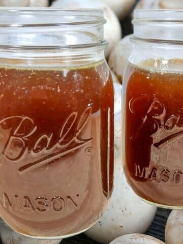 Jars of homemade mushroom stock overlaid on sliced mushrooms.
