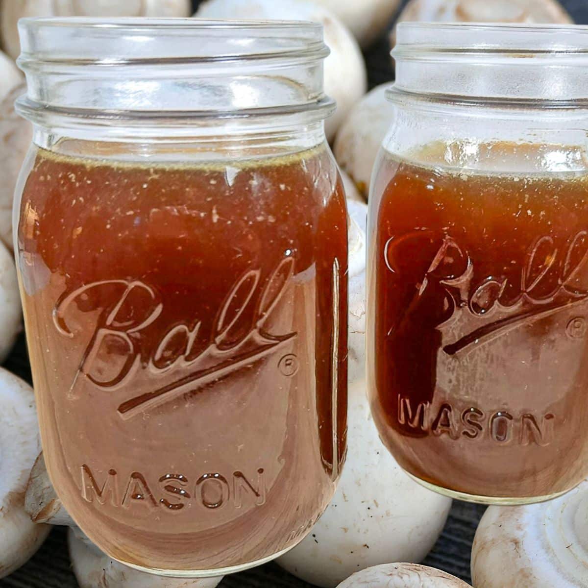 Jars of homemade mushroom stock overlaid on sliced mushrooms.