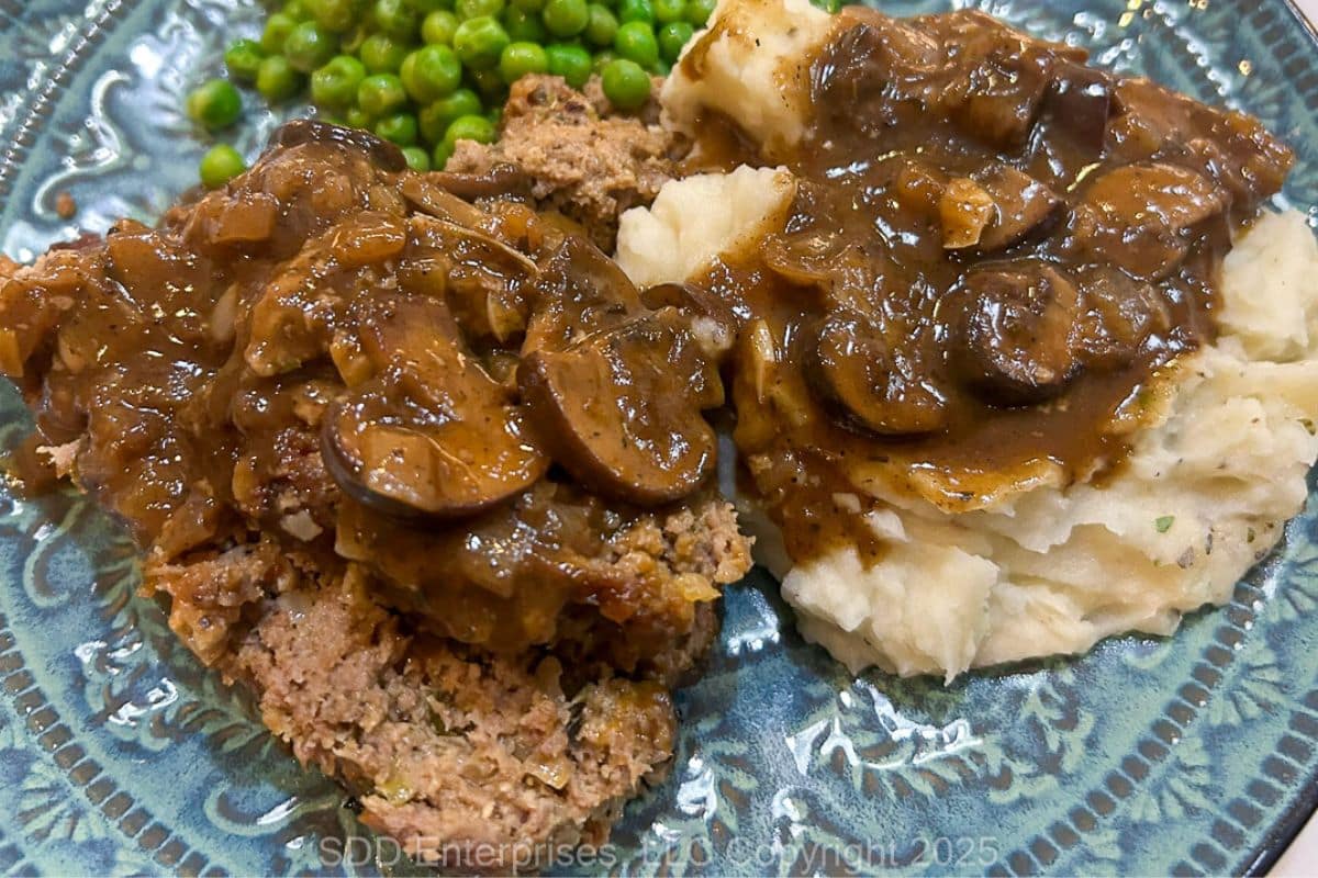 Meatloaf and mashed potatoes with mushroom gravy on a plate with sweet peas.