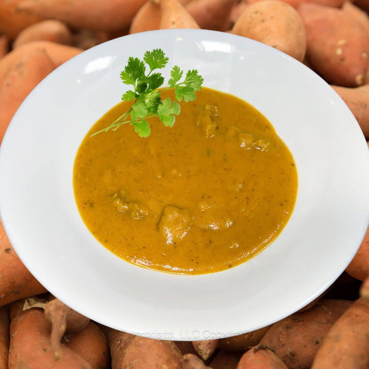 Sweet Potato Bisque with garnish in a white bowl overlaying fresh sweet potatoes.