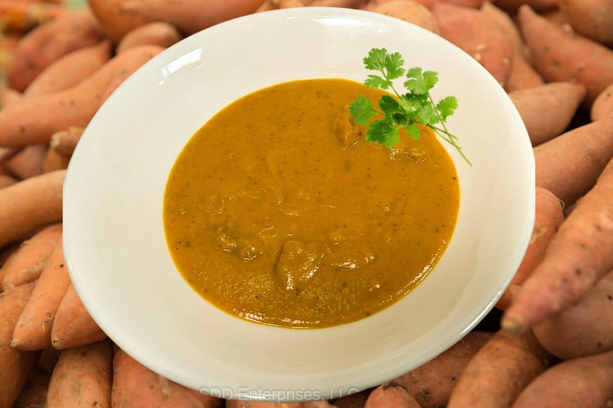 Sweet Potato Bisque with garnish in a white bowl overlaying fresh sweet potatoes.