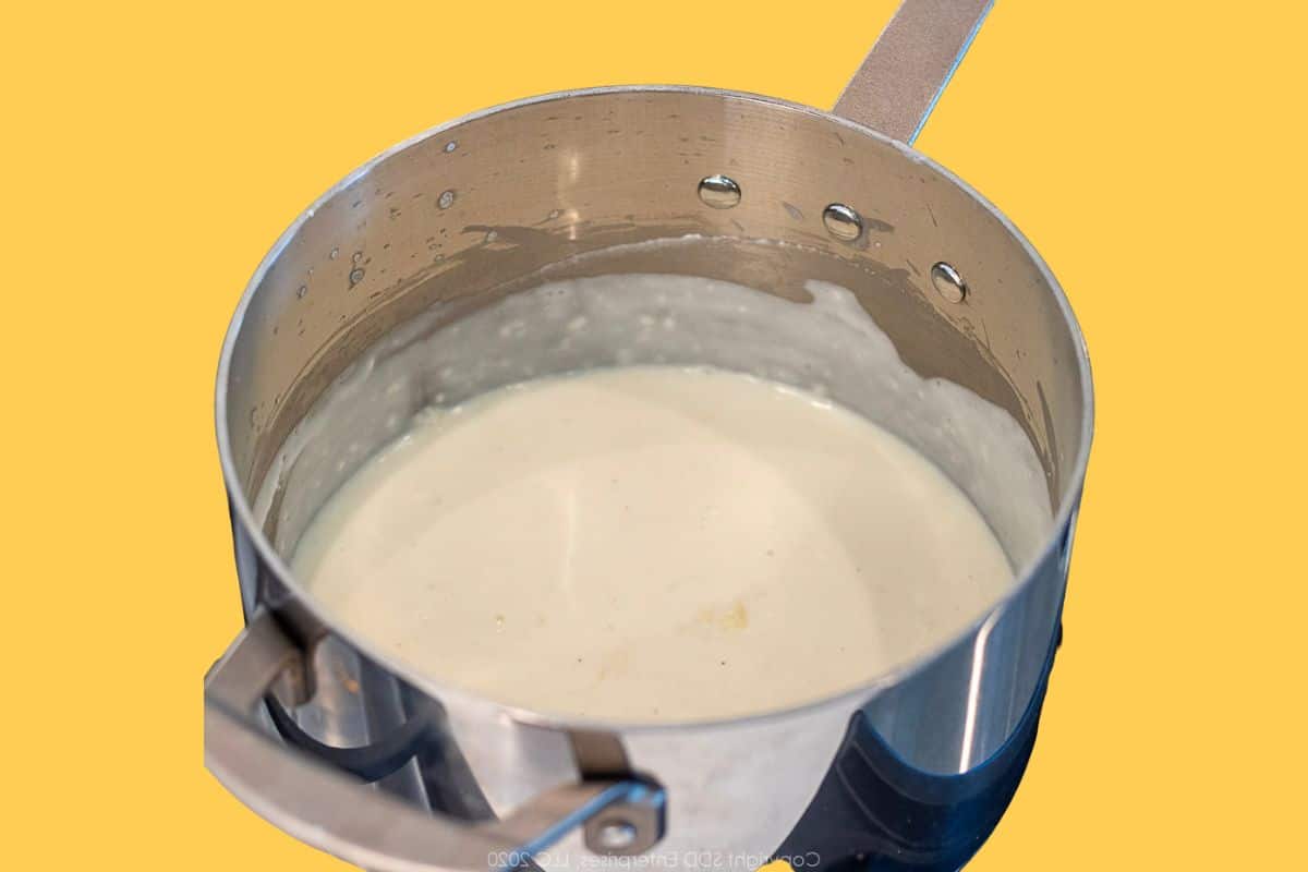 Smooth, creamy béchamel sauce simmering in a stainless-steel saucepan, showing its velvety texture.