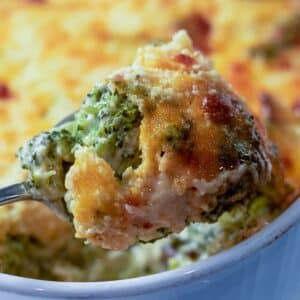 A spoonful of Broccoli Cheese Casserole right out of the baking dish overlaid on fresh broccoli.