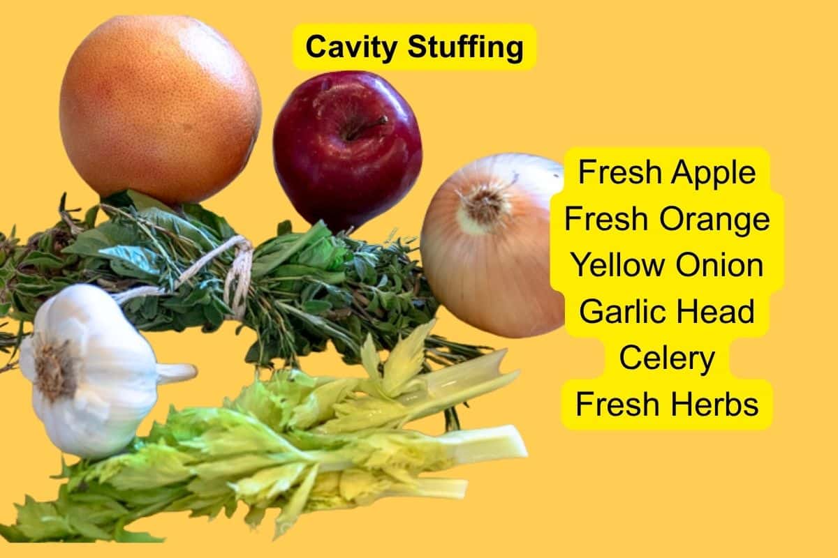 Fresh apple, orange, yellow onion, garlic head, celery, and a tied bundle of fresh herbs arranged for turkey cavity stuffing.