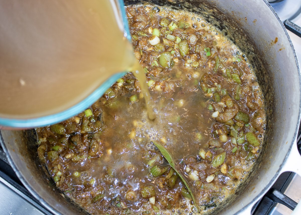 Adding homemade shrimp stock to a roux with vegetables.