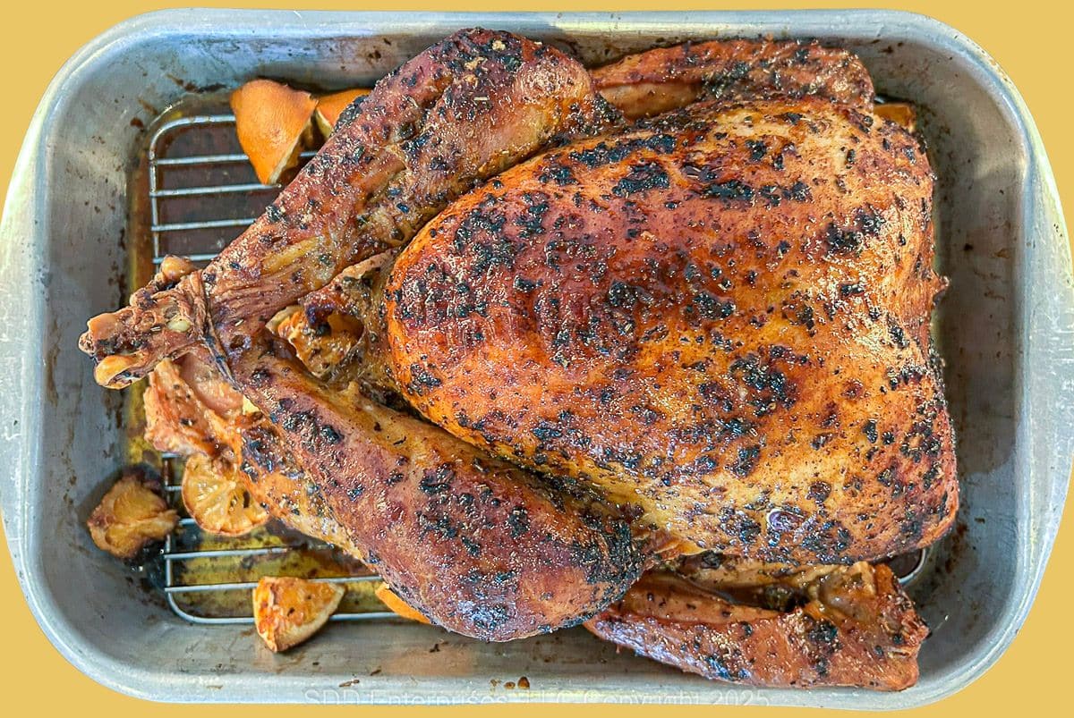 A whole herb-roasted turkey on a cutting board, stuffed with apples and herbs, surrounded by fresh parsley.