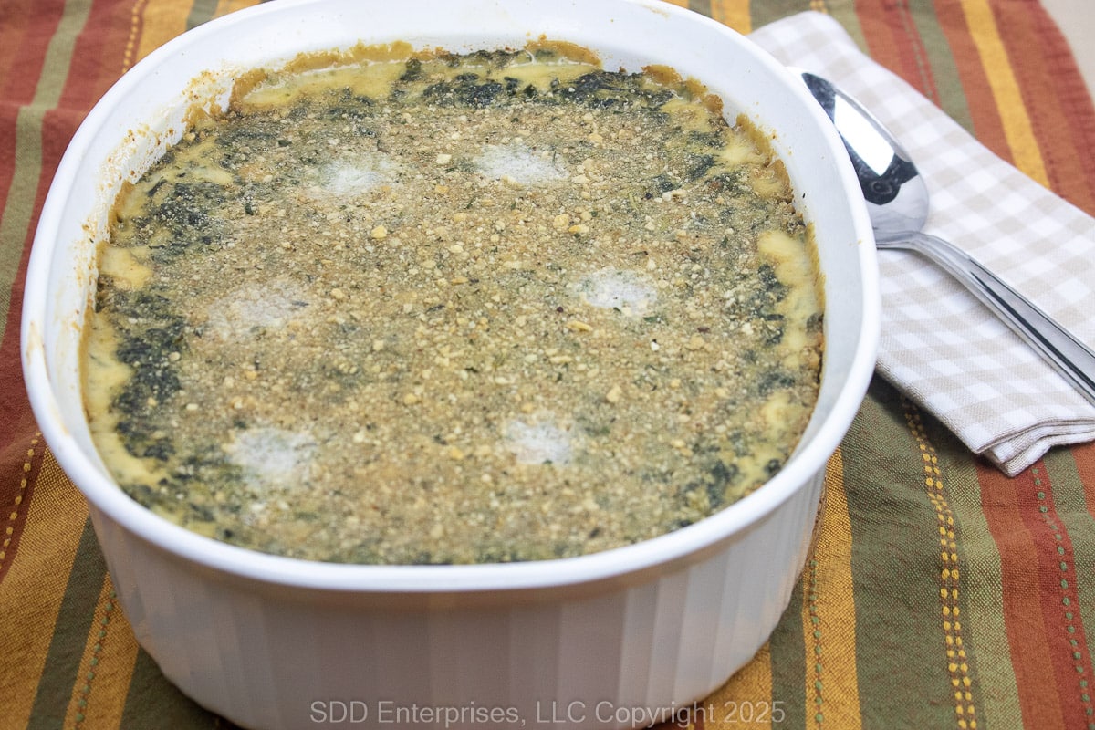 Spinach Madeleine in a white baking dish with a napkin and spoon on the side.