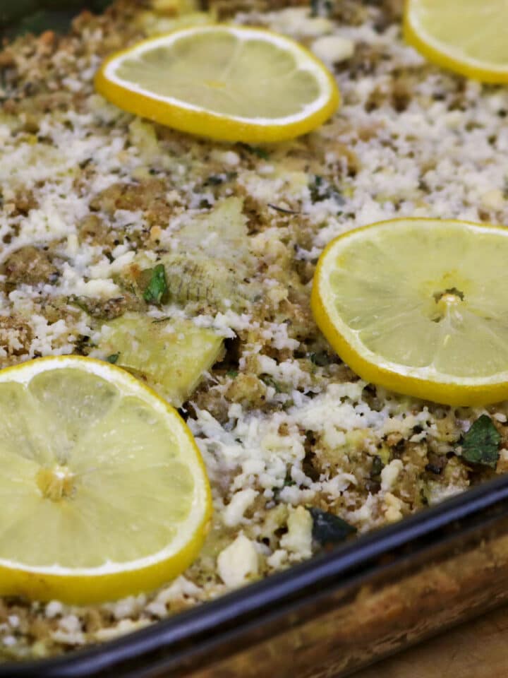 Stuffed Artichoke Casserole in a baking dish garnished with lemon slices.