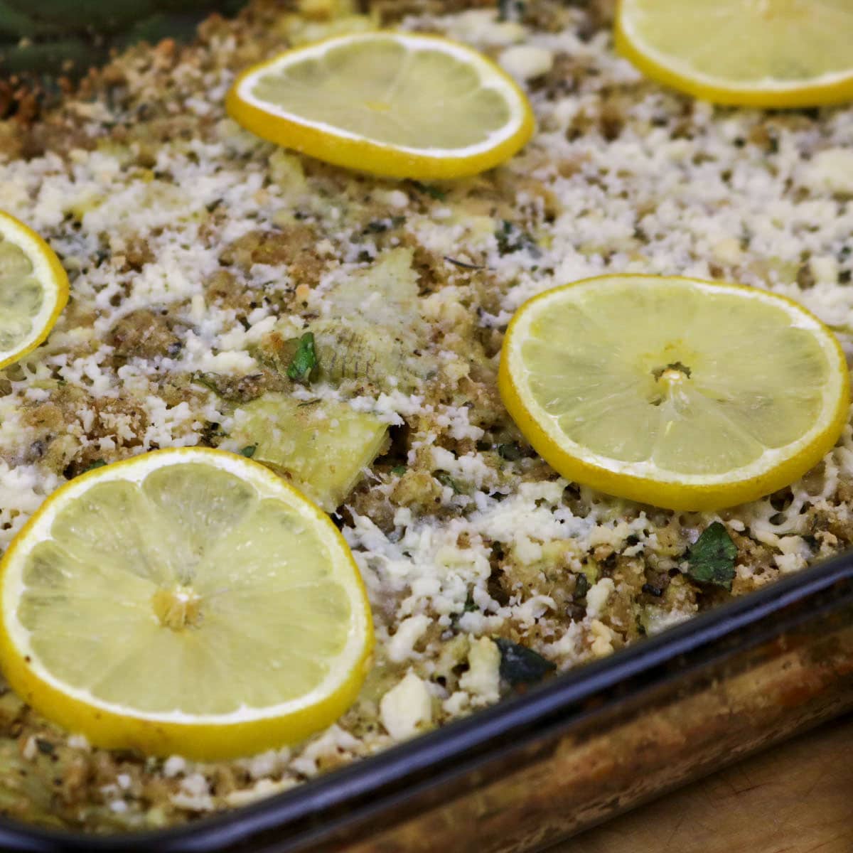Stuffed Artichoke Casserole in a baking dish garnished with lemon slices.