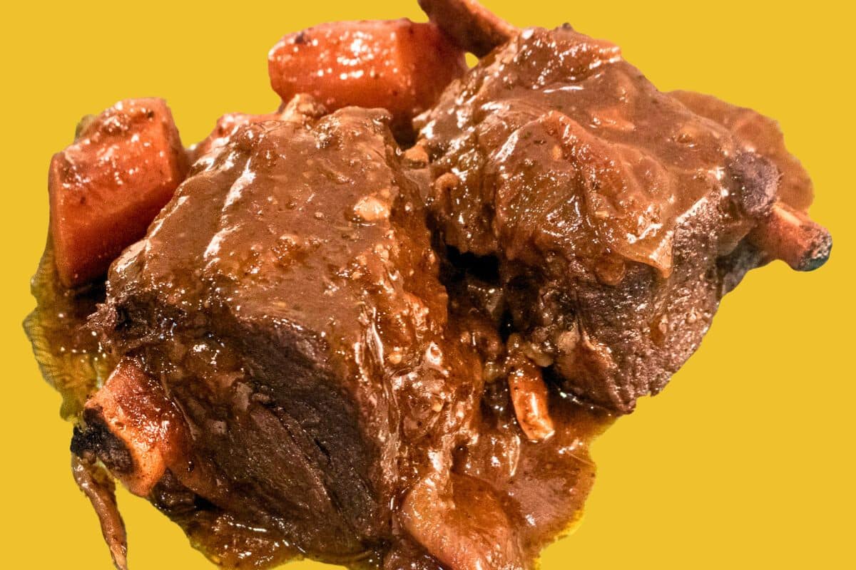 Braised beef short ribs with carrots on a gold back ground.