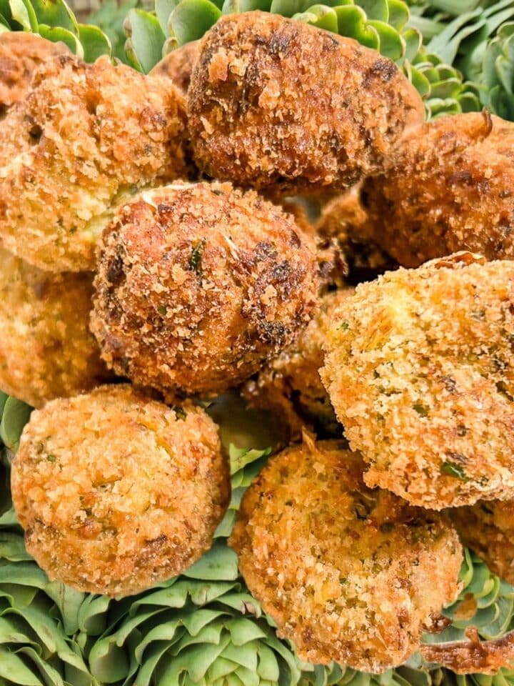 Fried Stuffed Artichoke Balls over a background of fresh artichokes.