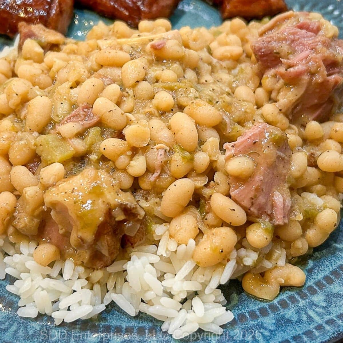 White Beans and Ham over white rice with a side of smoked sausage on a serving plate.