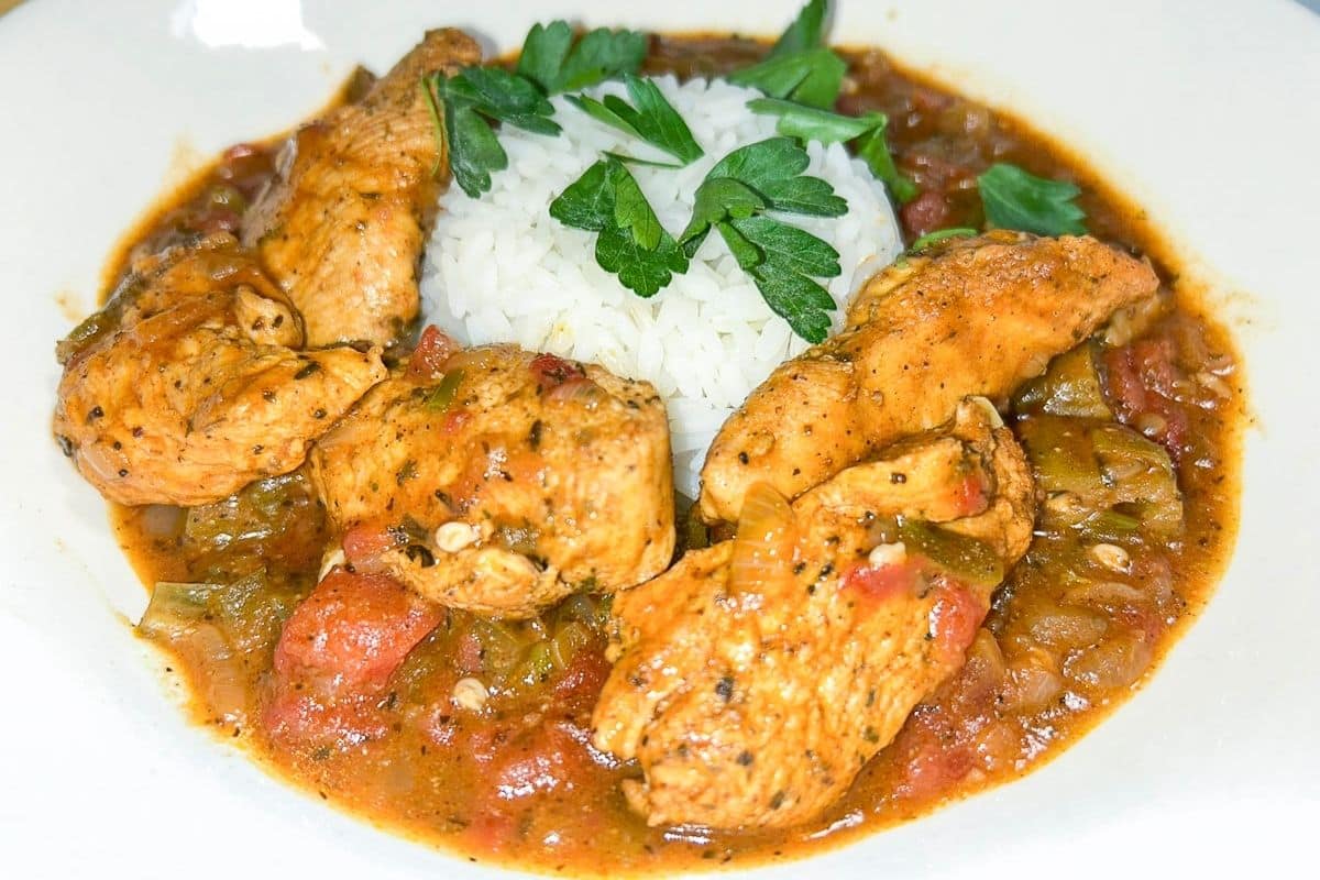 Chicken Creole served with rice in a white bowl garnished with parsley.