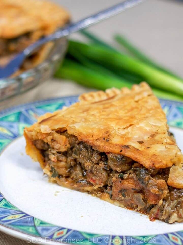 A slice of Crawfish Pie with a pie and garnish in the background.