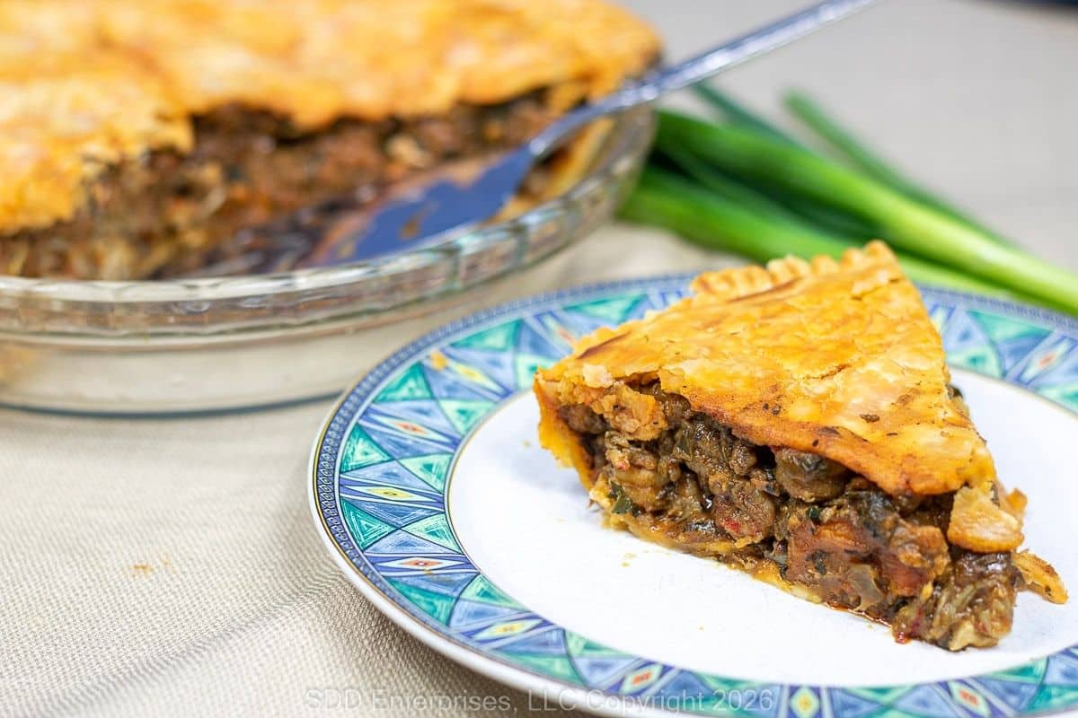 Crawfish pie with golden flaky crust sliced and served on a plate.