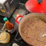 Red Beans simmering in a Dutch oven with hots sauce on a kitchen counter.