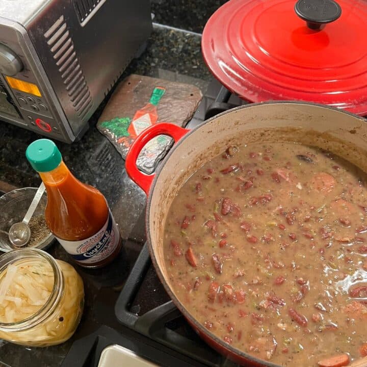 Red Beans simmering in a Dutch oven with hots sauce on a kitchen counter.