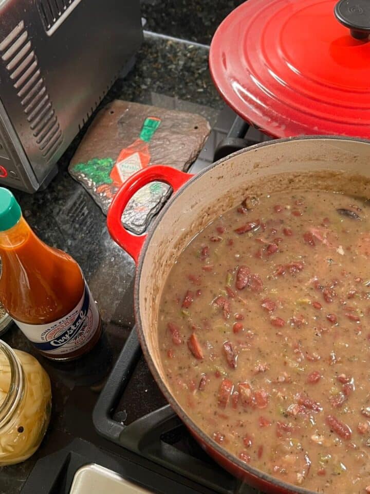 Red Beans simmering in a Dutch oven with hots sauce on a kitchen counter.