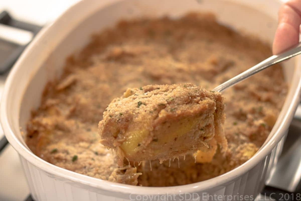Spoon lifting a serving of yellow squash casserole from the baking dish.