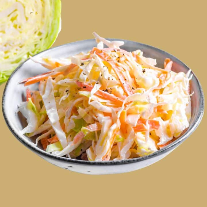 Creamy Coleslaw with Apple in a white serving bowl in from of a head of cabbage.
