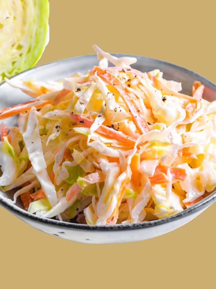 Creamy Coleslaw with Apple in a white serving bowl in from of a head of cabbage.