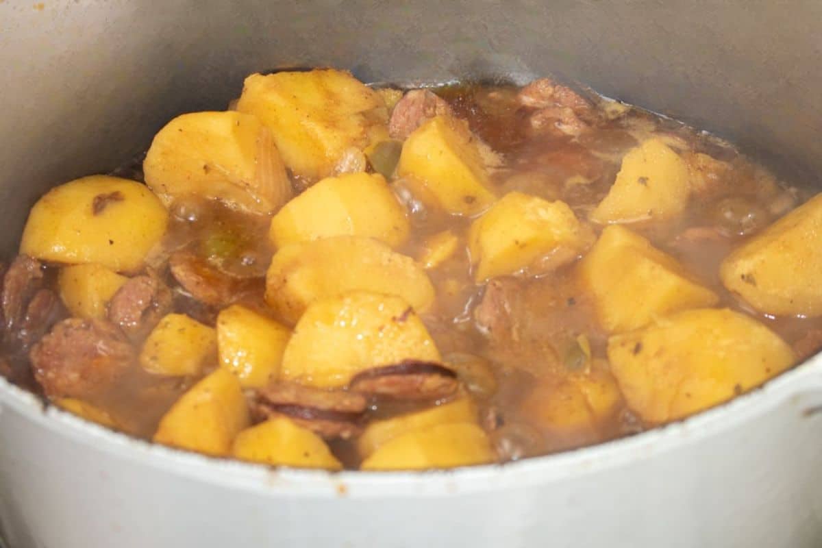 Smothered Yukon Gold potatoes and browned smoked sausage simmering in gravy in a Dutch oven.