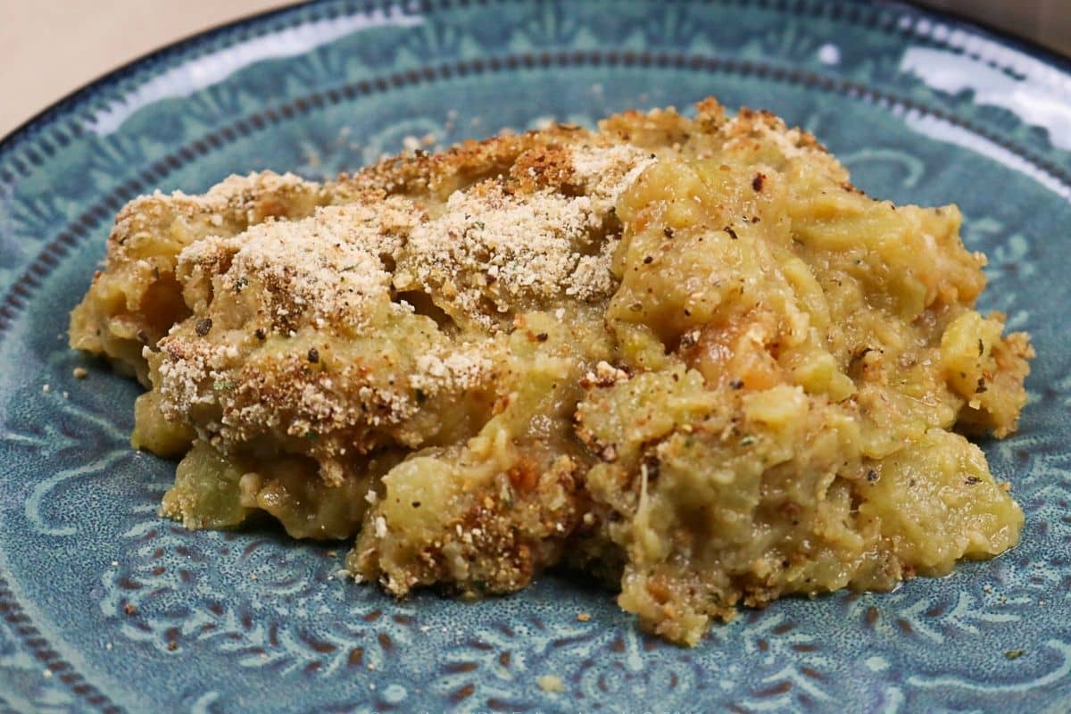 Close-up serving of mirliton casserole with a browned breadcrumb topping on a blue plate